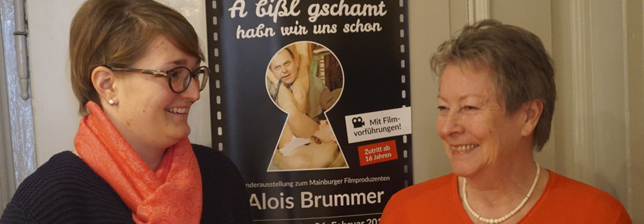 Museumsleitung und Mitwirkende vor Plakat zur Alois-Brummer-Ausstellung &quot;A bißl gschamt habn wir uns schon.&quot;