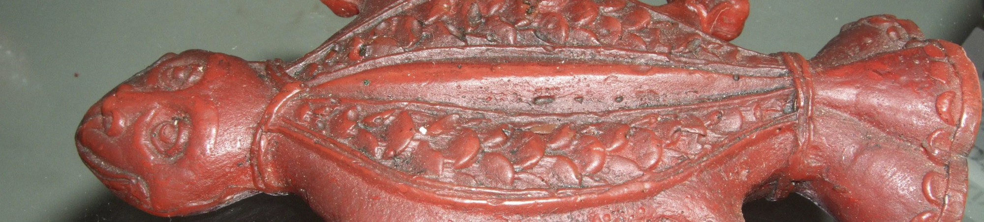 Stark stilisierte Darstellung einer Kröte. Der Kopf trägt menschliche Züge. Symetriscch angeordnete, kurze Beine. Auf der Bauchseite und auf dem Rücken geometrische Ornamente. Das hintere Ende ist wie eine Tülle geformt. Mit einer Model des 18. Jahrhunderts aus rotem Wachs gegossen. 