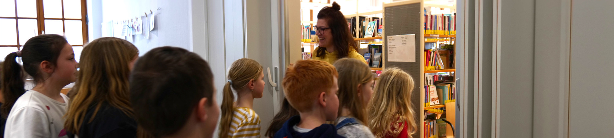 Kinder gehen durch die Schiebetür, die die Bibliothekarin geöffnet hat.