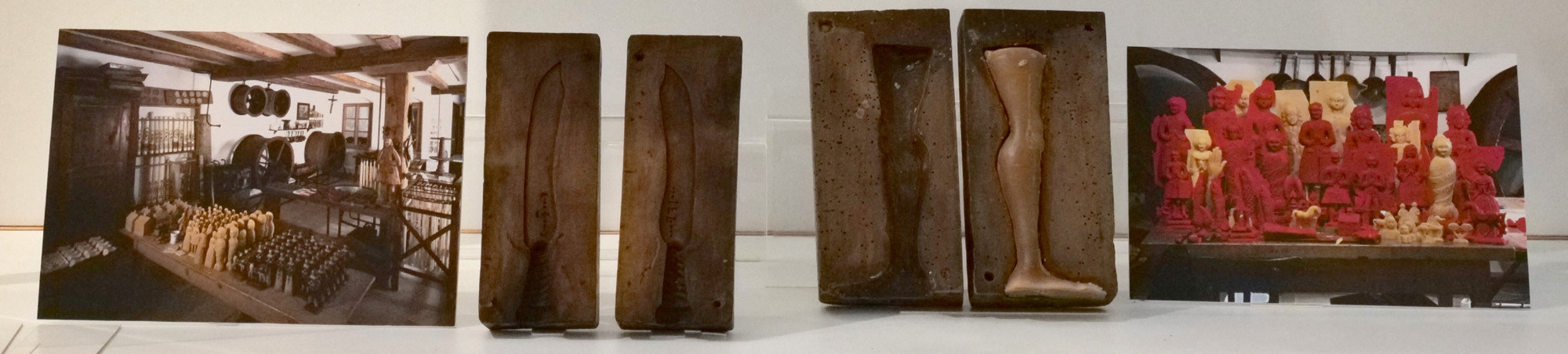 Von links nach rechts in der Vitrine: ein Werkstattfoto, Modelform für ein Messer, Modelform für ein Bein, Gruppenfoto von roten und haurfarbenen Votivabgüssen