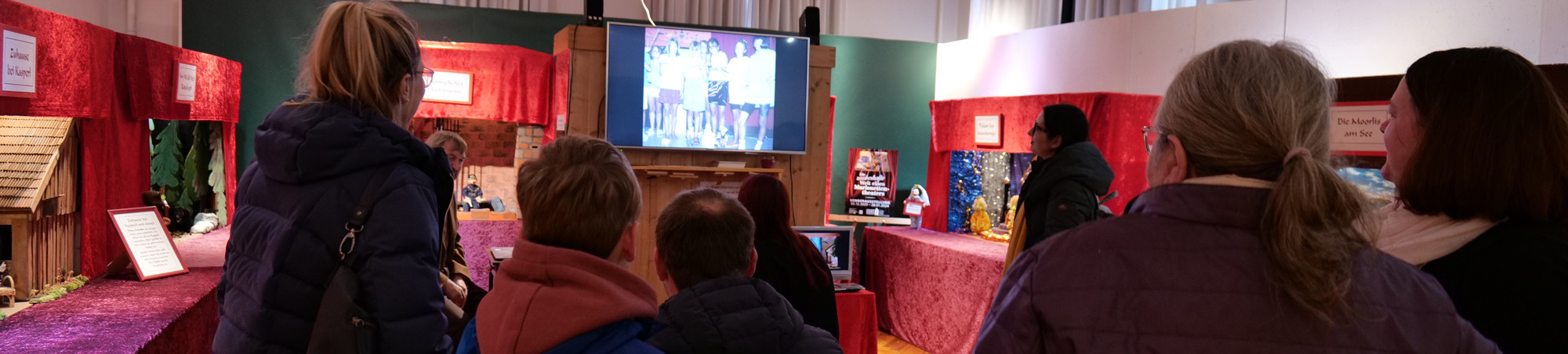 Der Kurator spielt Marionettenszenen auf einem großen Bildschirm ein und erläutert den Besuchern, wie Marionettentheater, gespielt von Schülern, funktioniert. Sch